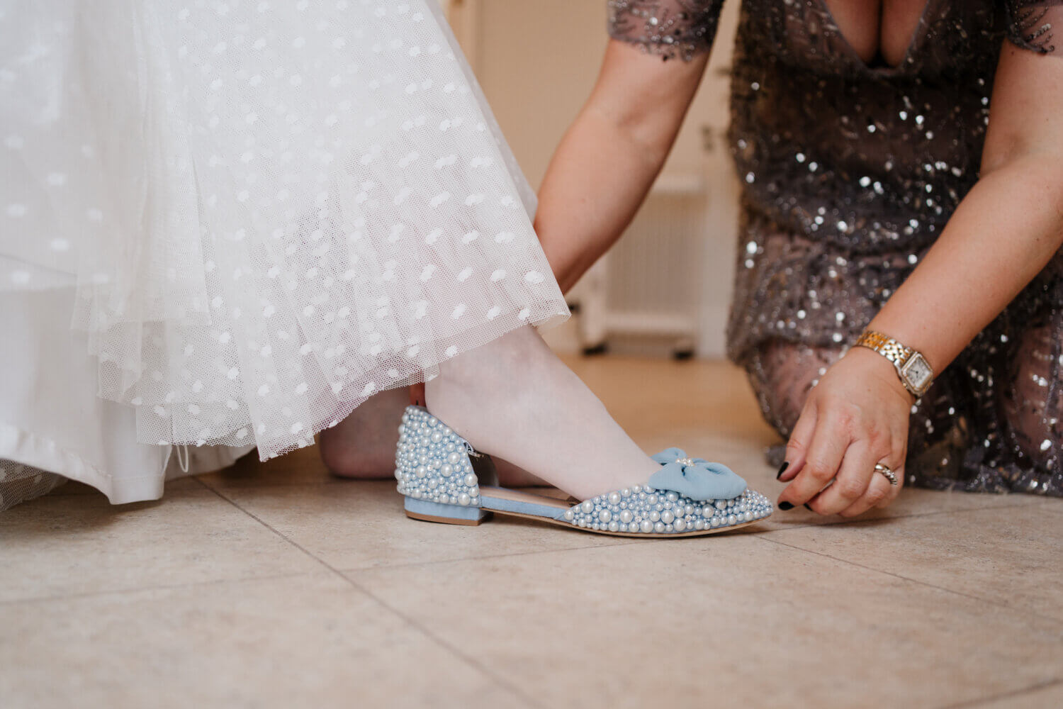 bride in ivory dress trying on blue pearly shoes