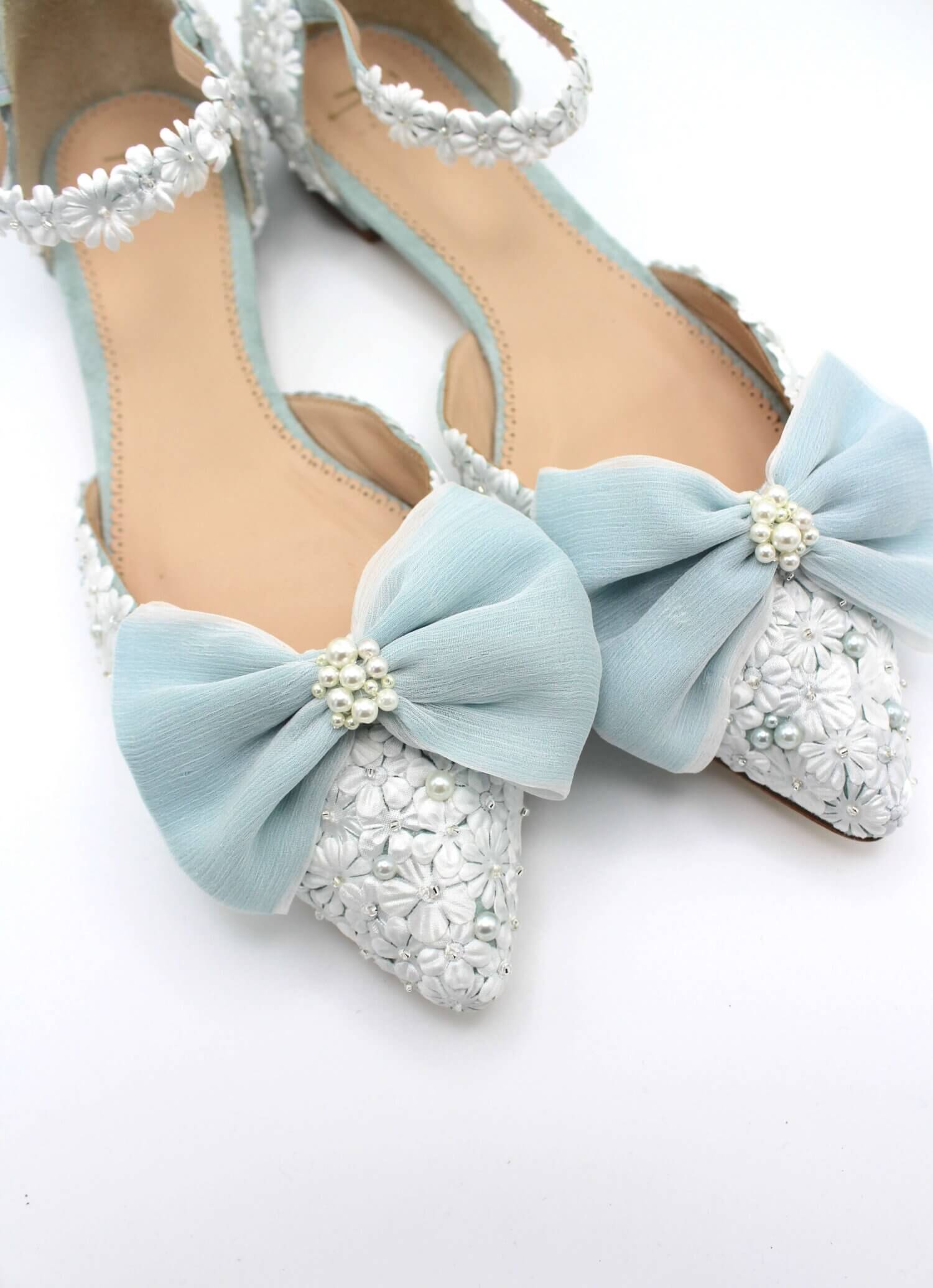 close up image of a pale blue and ivory shoe with floral details, pearls and blue chiffon bows